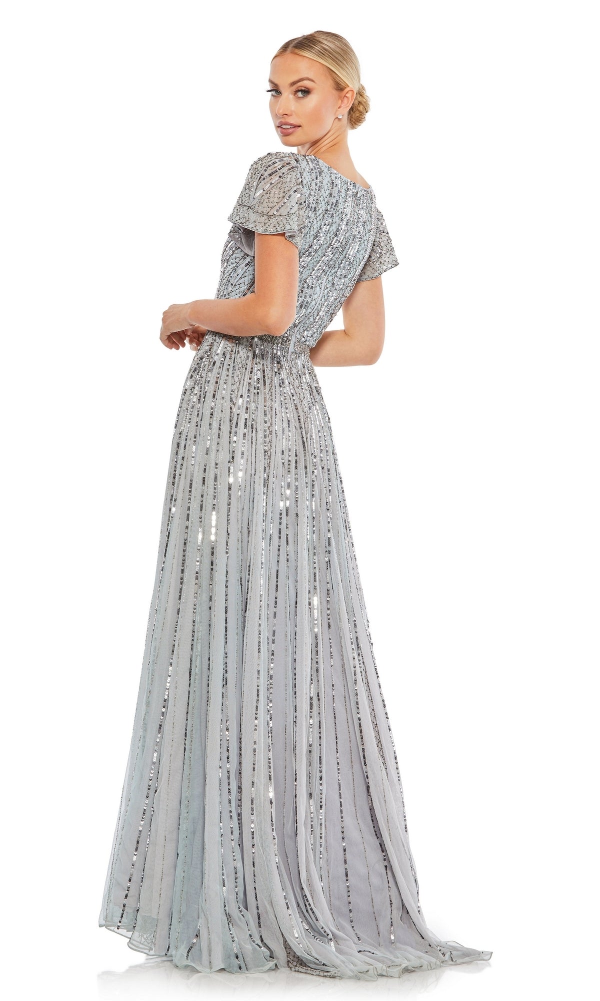 A woman in the Long Formal Dress 70108 by Mac Duggal, featuring a floor-length A-line silhouette, short sleeves, sequin details, V-neckline, and beaded belt, stands turned slightly away looking over her shoulder against a white background.